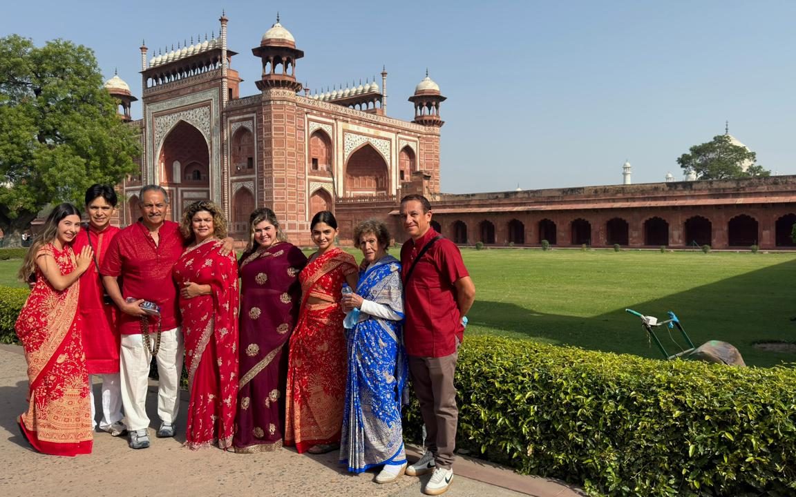 Un grupo de viajeros posando frente a la gran puerta de arenisca roja del Taj Mahal